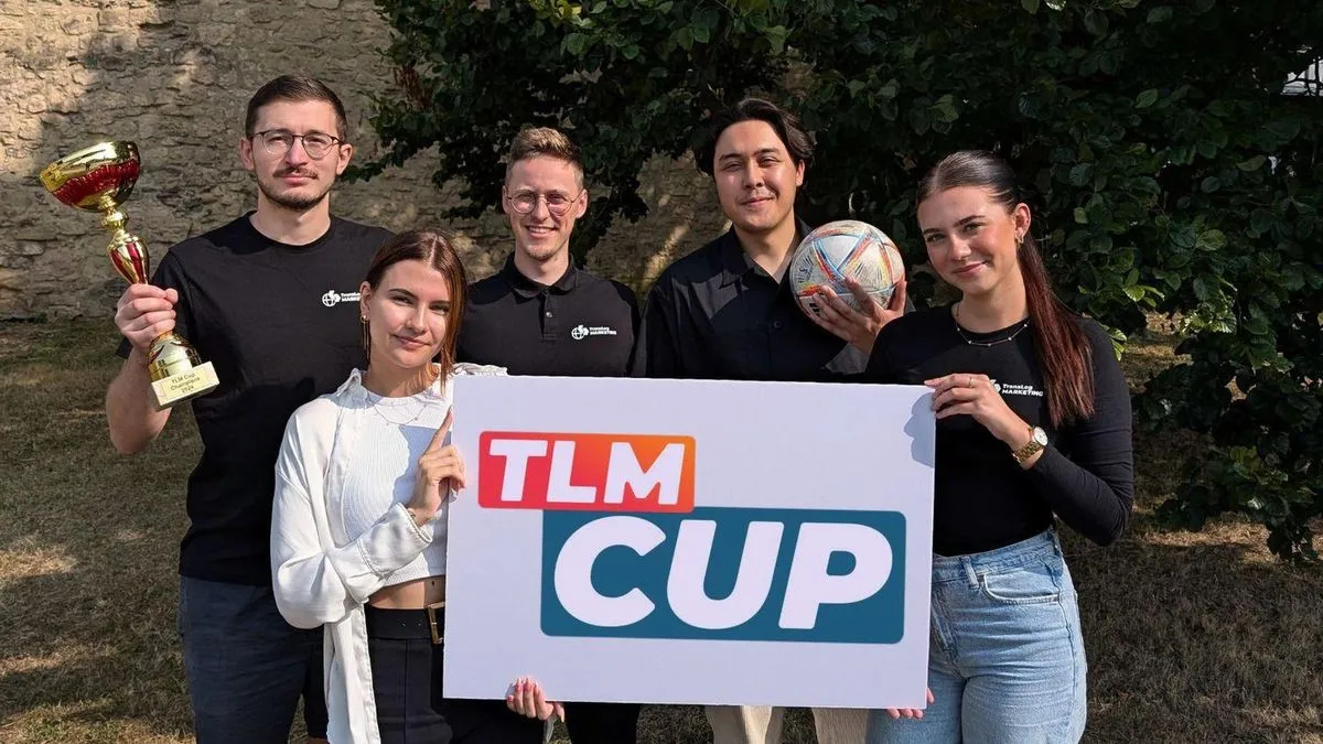Fünf aus dem TLM-Team mit Pokal, Fußball und einem Schild „TLM Cup“